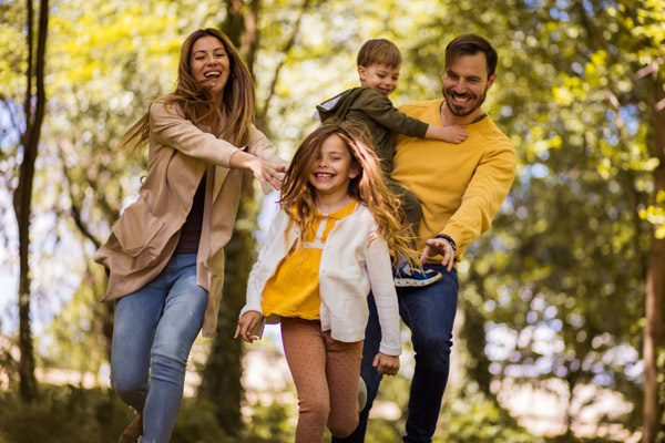 Eine Familie mit zwei Erwachsenen und zwei Kindern, die fröhlich im Freien laufen.