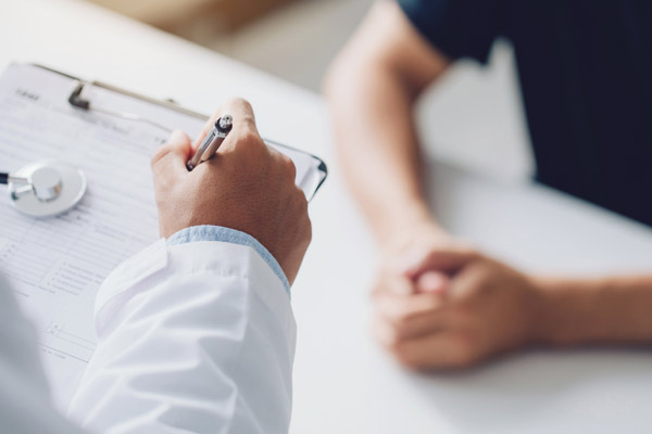 Ein Arzt schreibt auf einem Dokument, während ein Patient vor ihm sitzt.